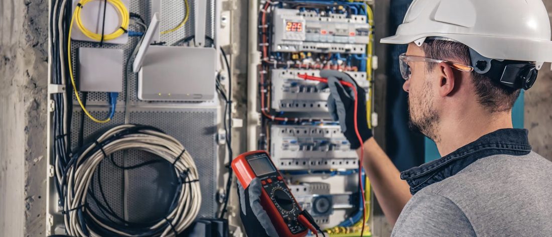 Electricista industrial con casco midiendo con multímetro un tablero eléctrico