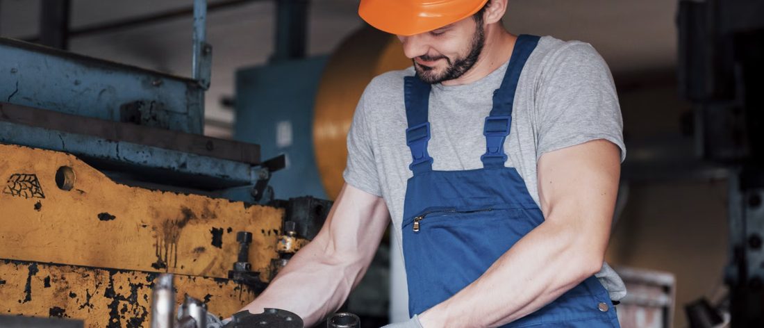 Técnico de mantenimiento con overol y guantes reparando una máquina industrial