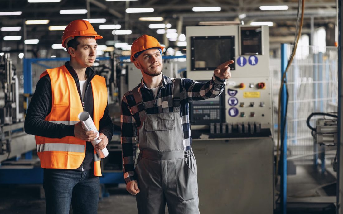 Dos técnicos con casco y chaleco revisando una máquina en planta